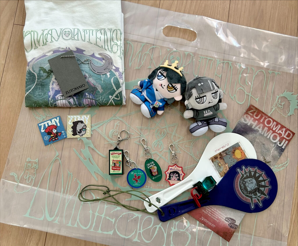 alt="ずとまよマート出張所で購入したTシャツ、ニラちゃんぬい、しゃもじ、しゃもじライト、ガチャガチャで当たったキーホルダー、エポスカード特典のステッカー"